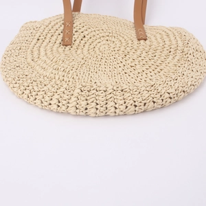 Detail of hand-woven straw bag featuring dark brown leather handles and cross-stitch seams