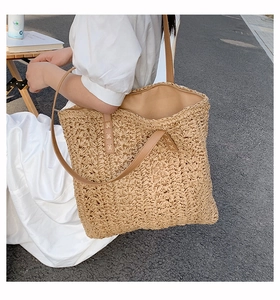 Close-up of a woven straw tote bag featuring brown leather straps and detailed texture