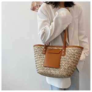 Detail view of woven straw tote bag with brown leather handles on a fashion model