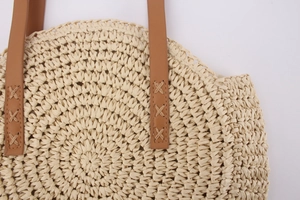 Close-up of woven straw bag showing reinforced brown leather handle and cross-stitching