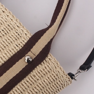Détail d'un sac en paille tressée beige avec sangle rayée et rivet métallique argenté