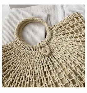 Detailed close-up of hollow mesh weave texture and round handle on straw beach tote bag