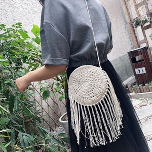 Detail of bohemian round straw bag with long fringes and woven cotton rope strap