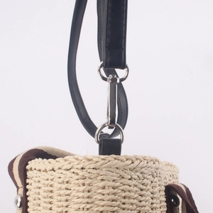 Détail de la texture tressée du sac en paille beige avec bandoulière en cuir noir et boucle métal