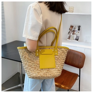 Detail view of woven straw tote bag with yellow leather straps and silver metal rivets