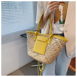 Detail of woven straw tote bag featuring yellow leather trim and adjustable shoulder strap