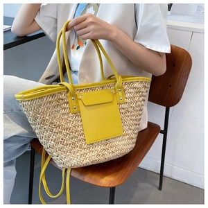 Detail of handwoven straw bag featuring yellow leather handles and adjustable shoulder strap