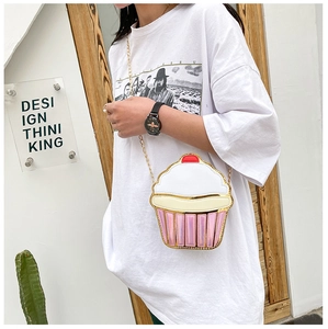 Close-up of a pink cupcake crossbody bag with gold chain strap in a natural setting