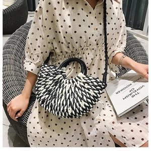 Detail of black and white straw bag with round handle and shoulder strap on a model