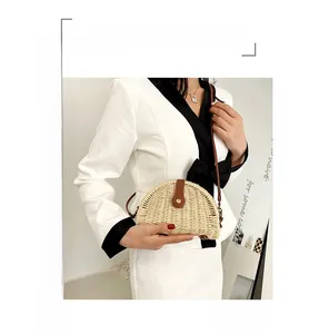 Detail of a handmade semi-circular woven straw shoulder bag with a brown leather clasp