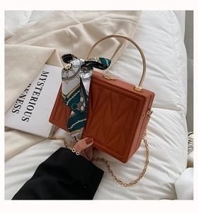 Detail of caramel box bag with quilted embroidery, silk scarf and gold metal handle