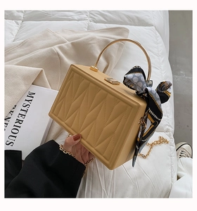 Detail of beige box bag featuring geometric quilting, gold handle and polka dot silk scarf