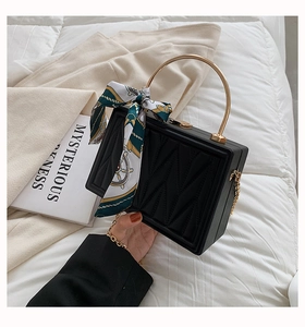 Detail of a black quilted box bag with a golden handle and silk scarf accessory