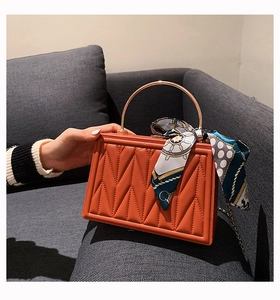 Detailed view of orange quilted leather box bag with gold handle and printed silk scarf