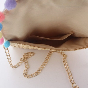 Detail of straw bag interior featuring soft fabric lining, inner pocket and colorful pom-poms