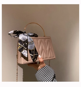 Detail of quilted beige box bag featuring gold chain strap and decorative silk scarf