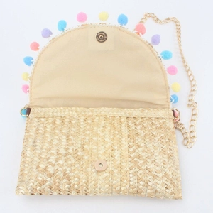 Detail of straw woven crossbody bag with colorful pom-poms and gold chain strap