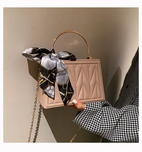 Close-up of quilted beige handbag featuring gold ring handle and decorative silk scarf