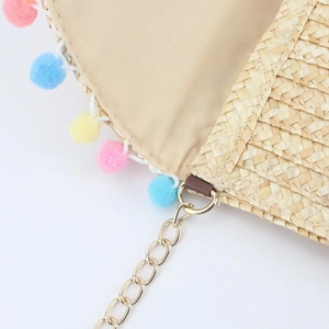 Detail of straw woven bag with colorful pom-poms and gold metal chain strap