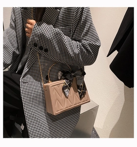 Detail of beige box handbag featuring V-quilted texture and silk scarf on handle