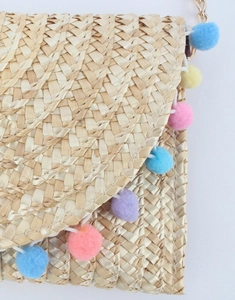 Close-up of handmade straw envelope bag with colorful pompom trim and gold chain