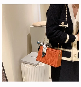 Detail of orange quilted leather handbag with gold ring handle and silk scarf