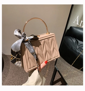 Detail of beige quilted handbag with gold metal handle and elegant silk scarf accessory