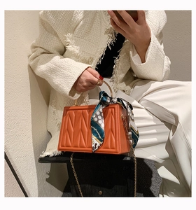 Detail of orange box bag with M-embossing, gold handle, and vintage polka dot scarf