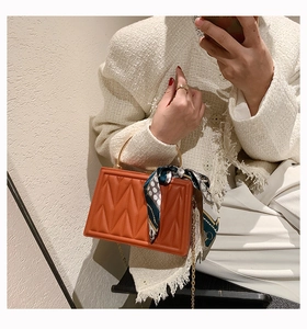 Close-up of orange quilted handbag with golden ring handle and elegant blue scarf detail