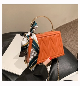 Detail of orange quilted PU leather handbag with silk scarf and gold ring handle