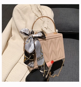 Detail of apricot quilted box bag with gold ring handle and patterned silk scarf accent