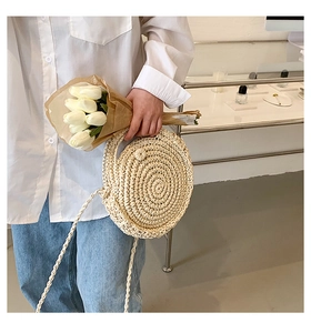 Detail of hand-woven round straw bag featuring a secure woven button closure and long strap