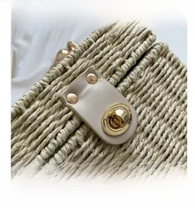 Detailed view of woven straw beach bag featuring golden metal turn-lock and beige leather trim