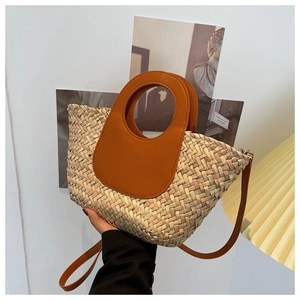 Detail of woven straw bucket bag with round cutout handle and tan leather shoulder strap