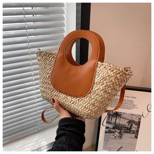 Detail of woven straw bucket bag with brown leather handle and thin crossbody strap