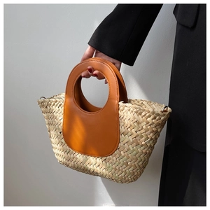 Detail of hand-woven straw bucket bag with brown leather handles and smooth texture