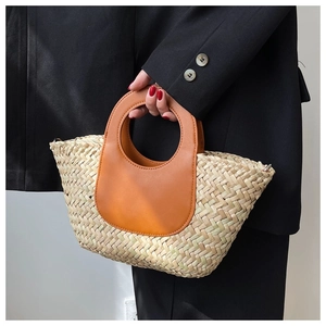 Detail of woven straw bucket bag with brown leather circular handle and wavy edge