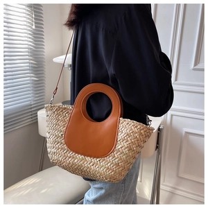 Detail of woven straw bucket bag with brown leather handles and a long shoulder strap