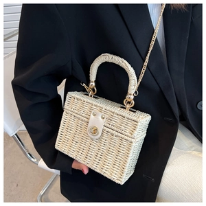 Detail of a beige straw woven box bag with metal lock and chain strap on a model