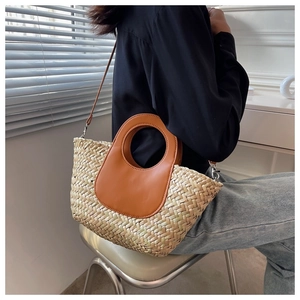 Detail of woven straw tote bag with brown leather handles and detachable shoulder strap