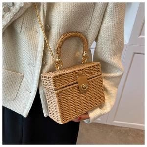 Detail of woven straw box bag featuring gold metal chain and brown leather clasp buckle