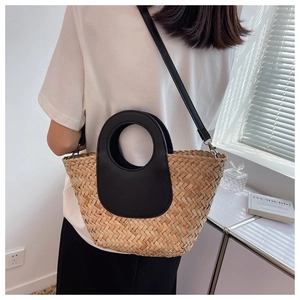 Straw bucket bag with black leather round handles and strap shown worn by a model