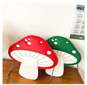 Detail of red and green mushroom shaped crossbody bags with metal chains on a wooden desk