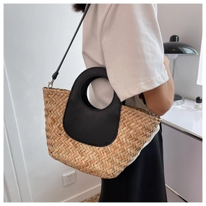 Detailed view of the straw bucket bag with black leather ring handles and woven texture