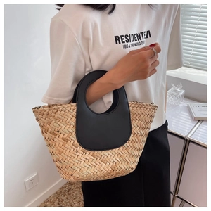 Detail view of woven straw handbag with contrasting black leather handle and stitching