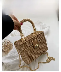 Detail of khaki woven straw box bag featuring a brown faux leather strap and golden clasp