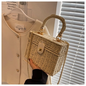 Detail of hand-woven straw box bag with golden metal chain and round top handle