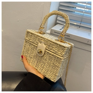 Detail of hand-woven straw box bag featuring gold hardware and a white leather clasp
