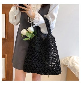 Detail of black crochet tote bag with mesh knit pattern and woven handles holding roses