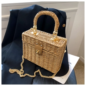 Detail of hand-woven straw box bag with brown leather accent and golden chain strap